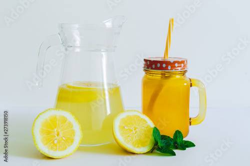 Lemonade pitcher and jar with cap placed on a white background – Healthy summer refreshment with lemon slices and mint leaves with copy space