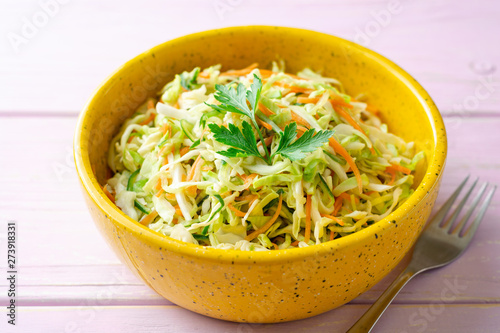 Coleslaw salad with cabbage, carrot and cucumber in bowl on purple wooden background. Selective focus.