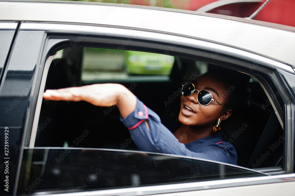 Rich business african woman on sunglasses sit at suv car and show hand from window.