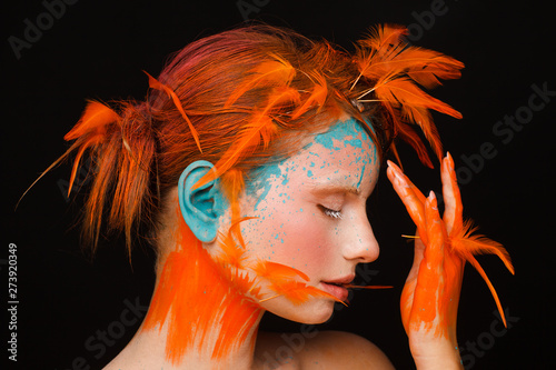 Fototapeta Portrait of a beautiful model with creative make-up and hairstyle using orange feathers
