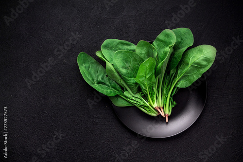 Fresh green spinach on a black plate on a dark background top view