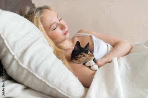 Young beautiful girl sleeping on bed with lovely kitten