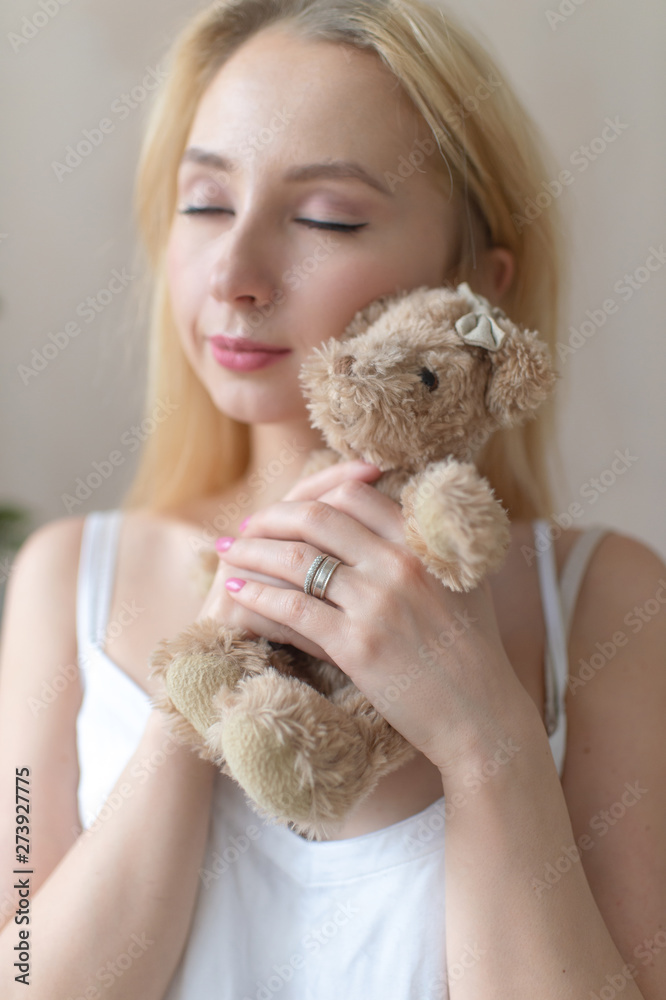 Young tender girl in nightie hugs toy bear.