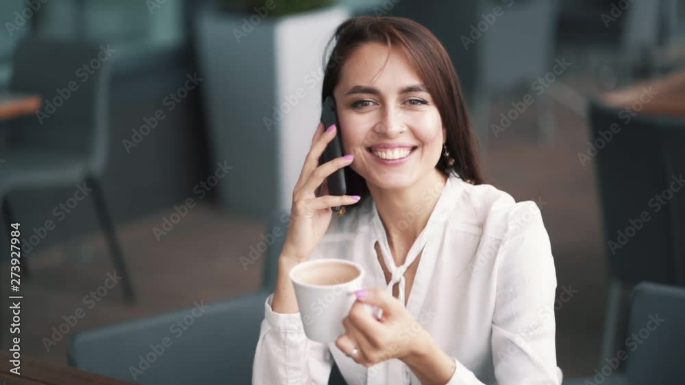Beautiful girl talks on phone, laughing and drinking coffee in cafe, slow motion Beautiful girl talks on phone, laughing and drinking coffee in cafe, slow motion