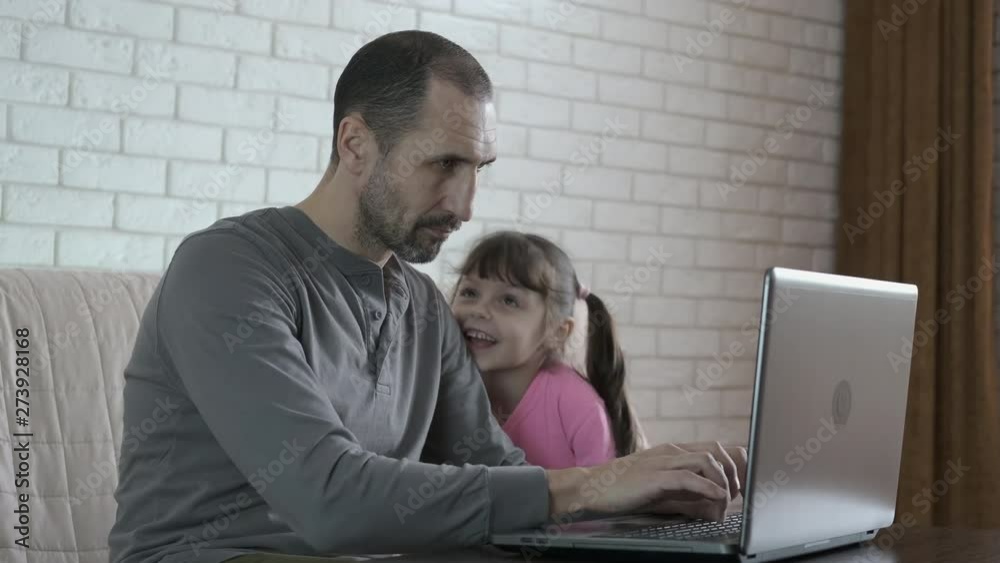 Father works at home. The child lacks parental attention. A little girl approaches her dad working on a laptop with the aim of playing with her, her father ignores her. Father works at home. The child lacks parental attention. A little girl approaches her dad working on a laptop with the aim of playing with her, her father ignores her.