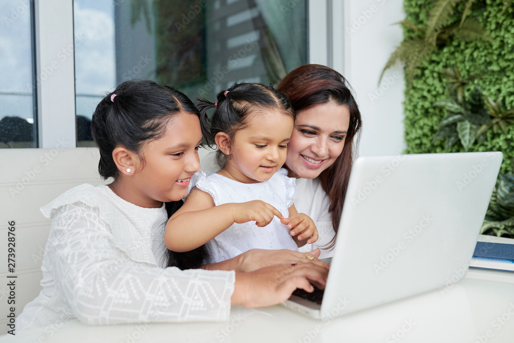 Smiling mother sitting together with her two children they looking at monitor of laptop computer and communicating online with their father