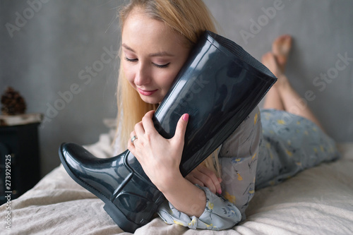 Strange woman hugs rubber boot on bed.