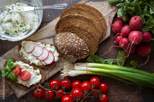 Preparation of summer sandwiches cottage cheese with green onions, radishes and tomatoes. keto diet ,healthy lifestyle. fresh fruit.On a dark background .wood boards