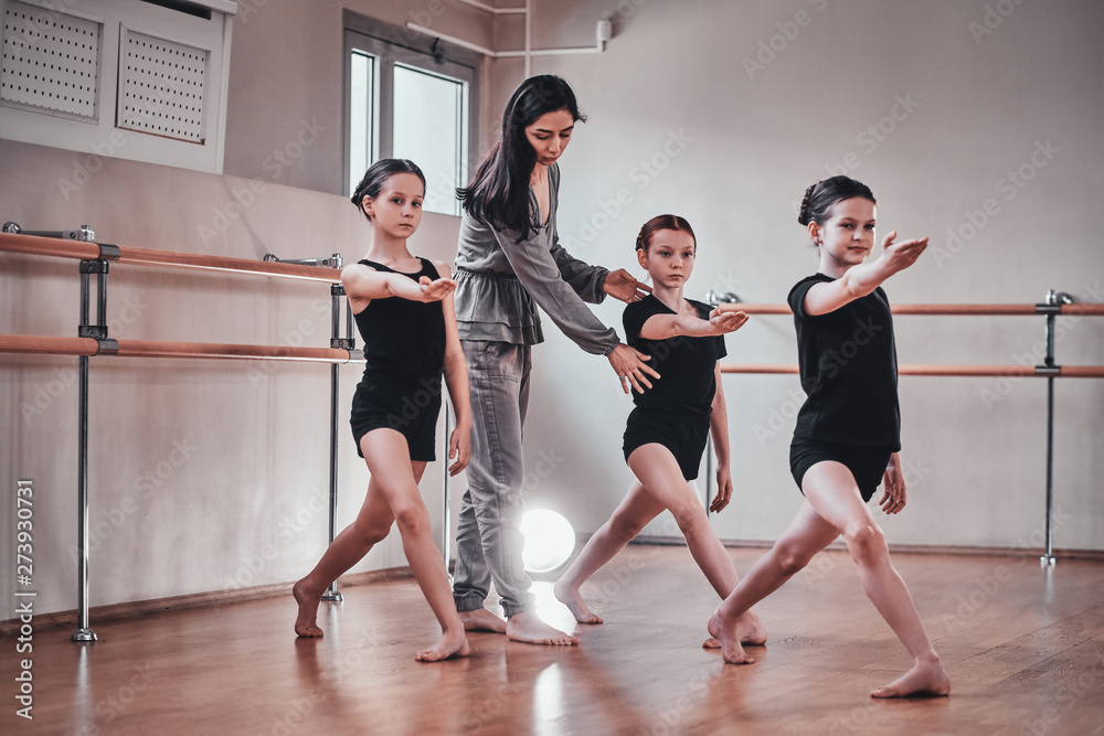 Obraz premium Three young diligent girls have a ballet training with their attractive teacher at bright training room.