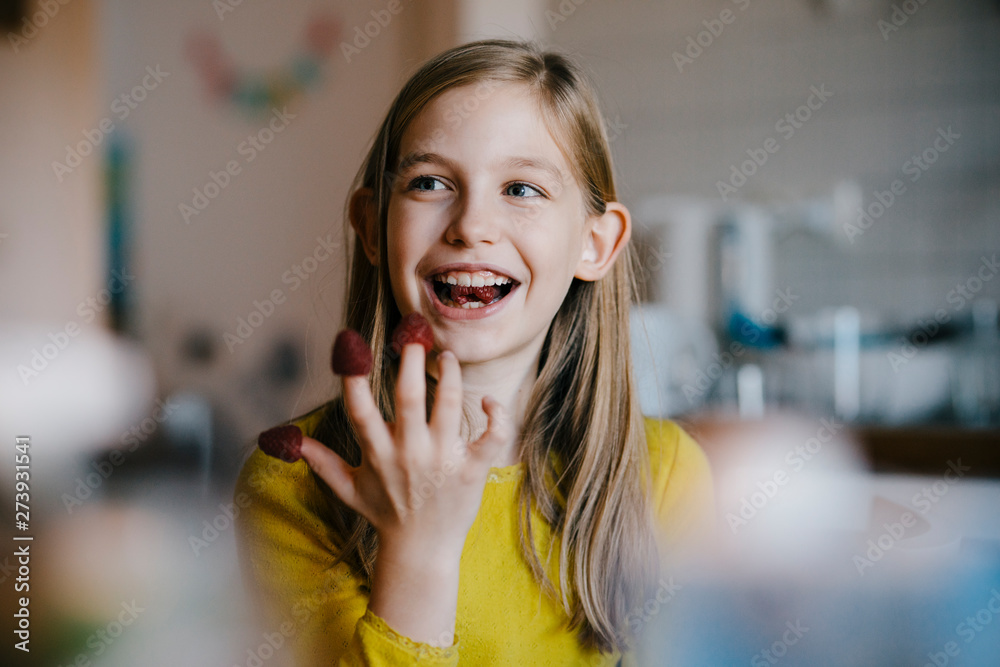 Happy girl sitting at kitchen table at home playing with raspberries Happy girl sitting at kitchen table at home playing with raspberries