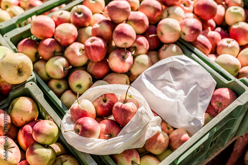 Cloth bag and plastic bag on boxes with apples on weekly market photo