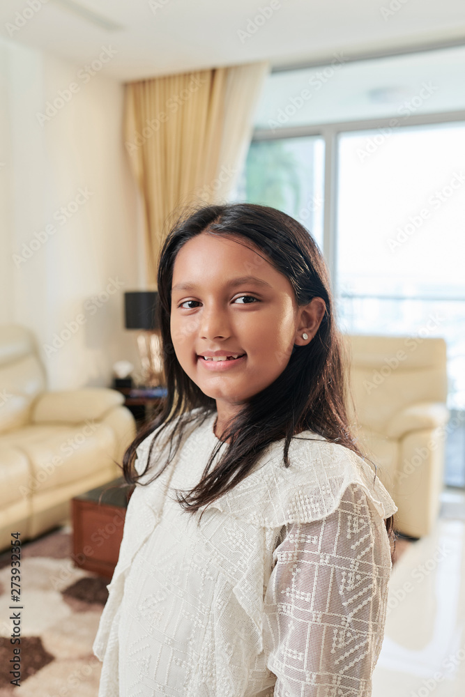 Portrait of Indian little girl with black long hair smiling at camera while standing in the living room at home Portrait of Indian little girl with black long hair smiling at camera while standing in the living room at home