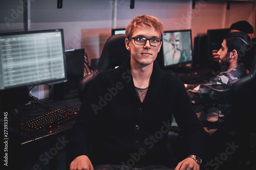 Portrait of blond young man in glasses at internet club playing videogames. photo