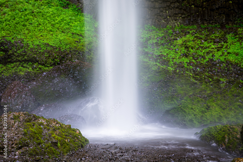 A beautiful waterfall splashing into a pool beneath rocks covered in lush green moss and vegetation - Latourell Falls in Oregon's Columbia River Gorge