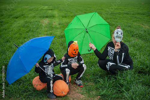 Girl mother with children in skeleton bone on green field with umbrella with pumpkins on eve of holiday Halloween