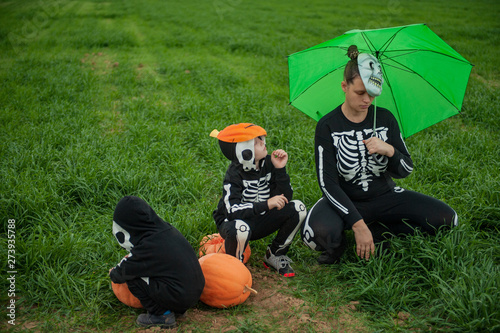 Girl mother with children in skeleton bone on green field with umbrella with pumpkins on eve of  holiday Halloween photo