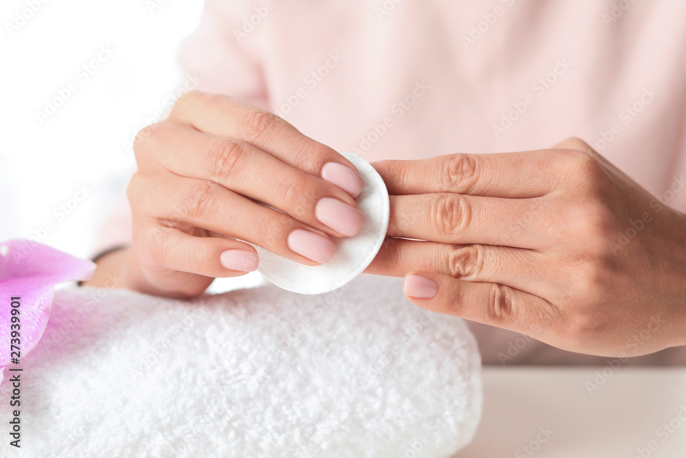Woman removing polish from nails with cotton pad at table, closeup