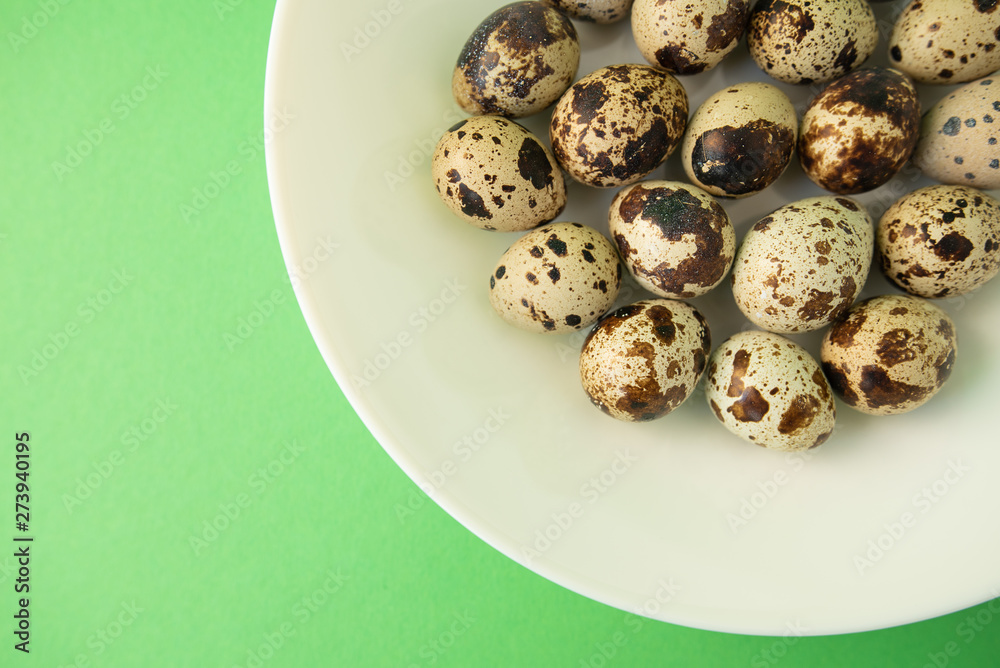 Raw quail eggs in white plate on green background. Easter. Raw quail eggs in white plate on green background. Easter.