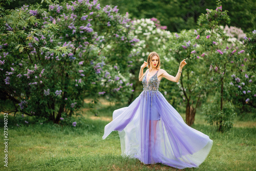 beautiful young happy girl in an incredible dress resting outdoors,woman walking in the park amid blooming lilacs