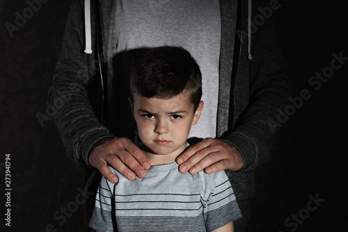 Scared little boy and adult man on dark background. Child in danger photo