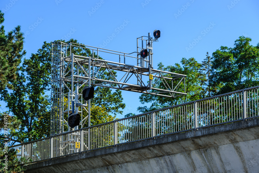 Train signals above bridge with fence.