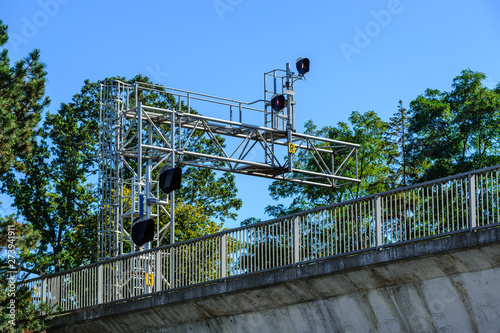 Train signals above bridge with fence.