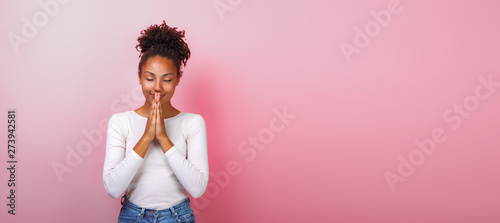 Portrait of woman in supplication pose with smile and close eyes over pink background. Copyspace