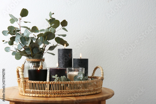 Tray with burning candles and green branches on table at white wall  space for text