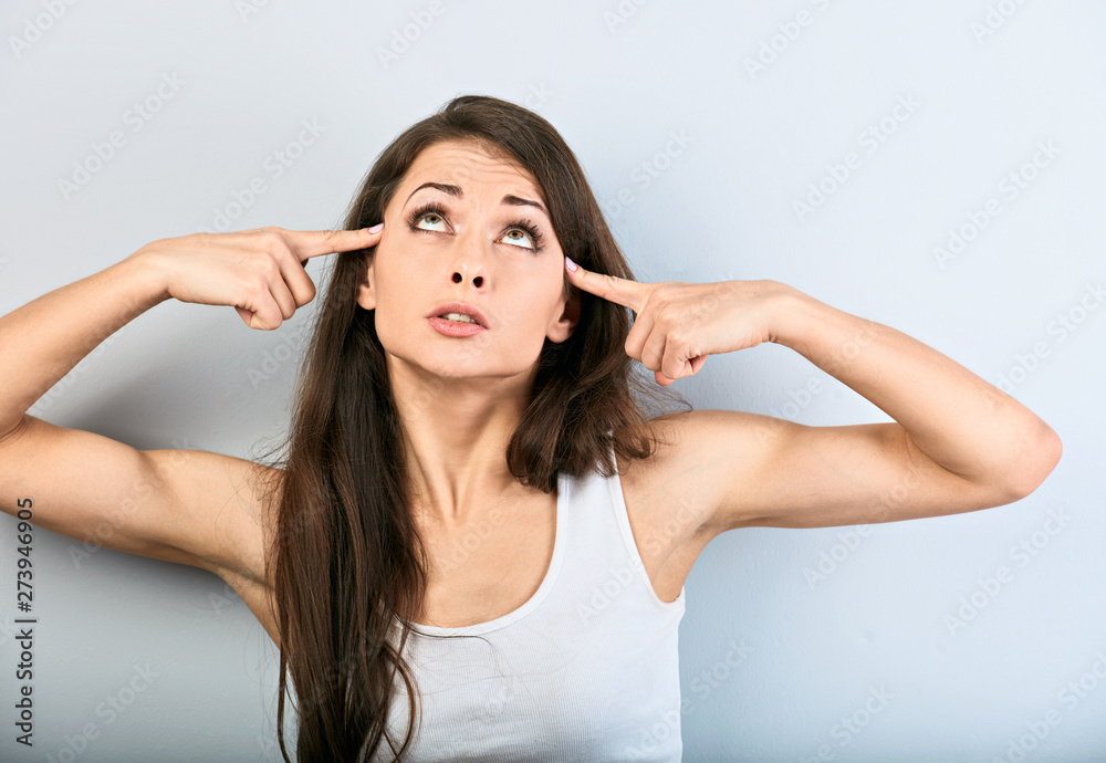 Young beauiful girl showing finger gun gesture, shooting herself and looking up on blue background. Closeup Young beauiful girl showing finger gun gesture, shooting herself and looking up on blue background. Closeup