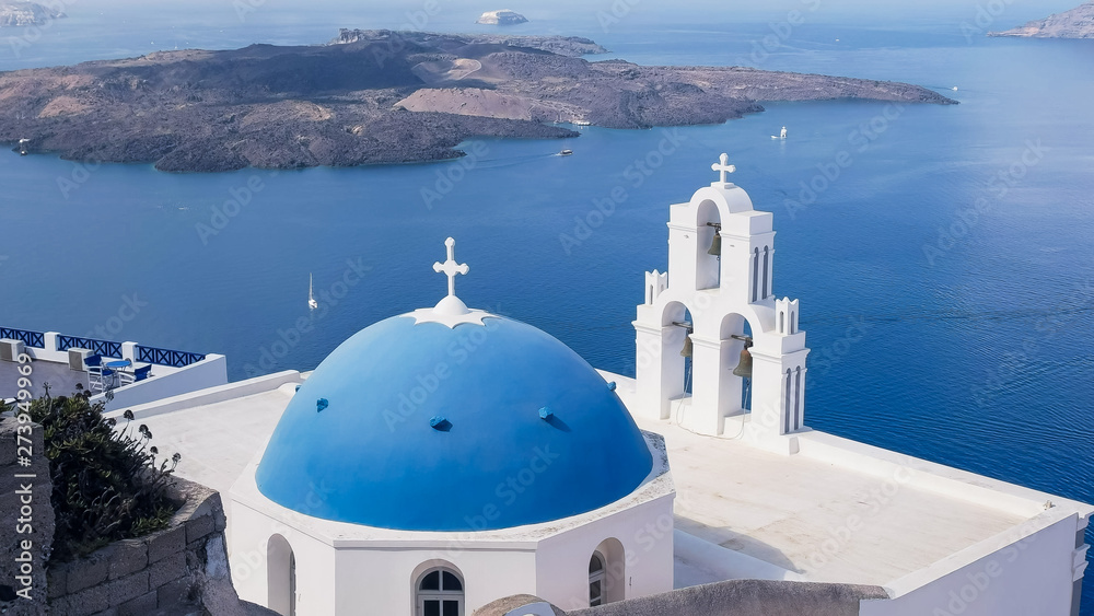 wide shot of a blue church dome and three bells in fira, santorini