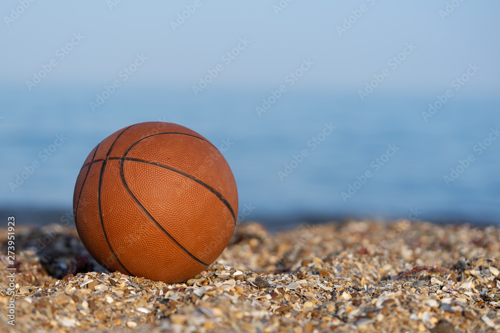 Basketball ball lying on the sand by the sea at sunset.