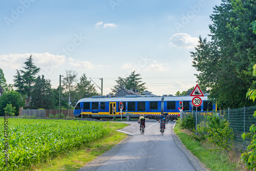 Obraz na plátně Outdoor sunny view of cyclists stop in front of level crossing railway barrier waiting for a train and green traffic light in small village countryside in Germany