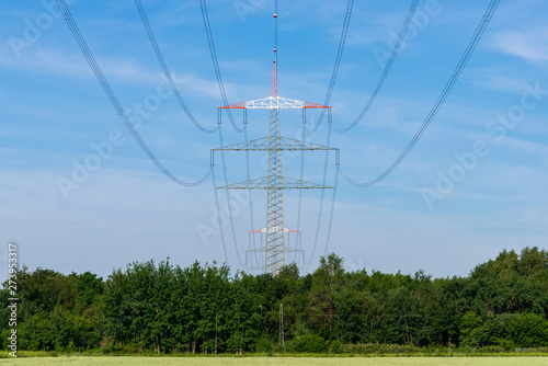 Outdoor sunny view of high voltage post and cable over range of tree and agricultural field in countryside  suburban area of Düsseldorf, in Meerbusch, Germany in summer season against deep blue sky. photo