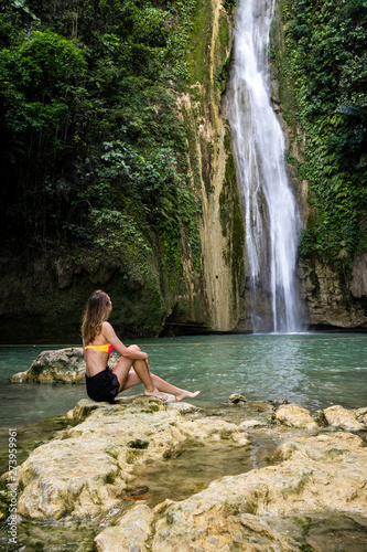 Girl sitting in front of Mantayupan Falls in Barili Cebu, Philippines in the morning