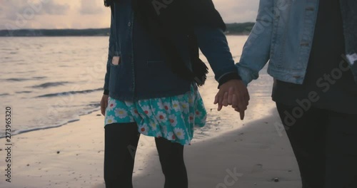 Two young women holding hands on the beach after sunset