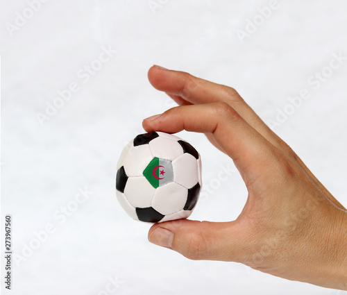 Mini ball of football in hand and one black point of football is Algeria flag, hold it with two finger on white background.