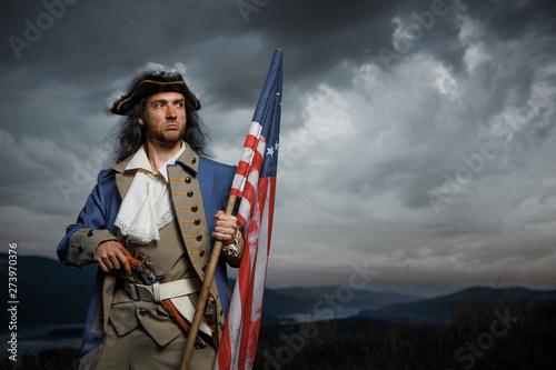 фотографія Soldier of United States War of Independence with flag and pistol posing over dramatic sky