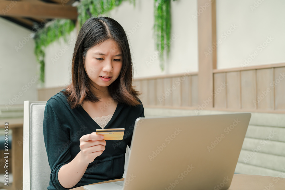 Closeup Asian beautiful woman Wearing a black shirt Sitting in the house Have a credit card in hand Is buying online products with a laptop computer Closeup Asian beautiful woman Wearing a black shirt Sitting in the house Have a credit card in hand Is buying online products with a laptop computer