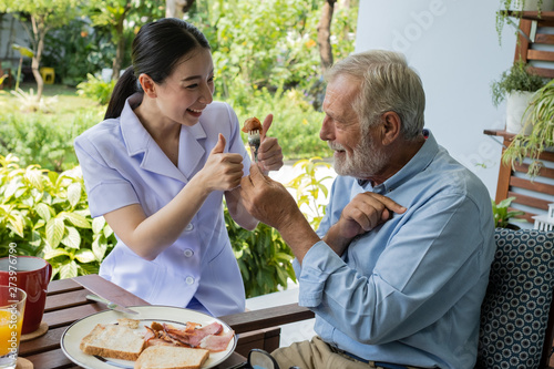 senior man happiness with smiling nurse, takes care breakfast at balcony near garden at nursing home