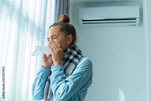 Fotografie Sneezing woman caught a cold from the air conditioner at home