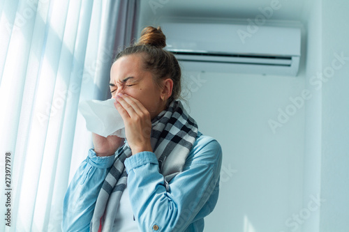 Sick sneezing woman in scarf caught a cold from the air conditioner at home.