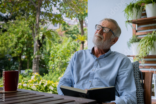 senior man happiness sitting and reading book at balcony near garden at nursing home for relaxing