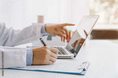 Doctor in hospital writing medical documentation and using laptop