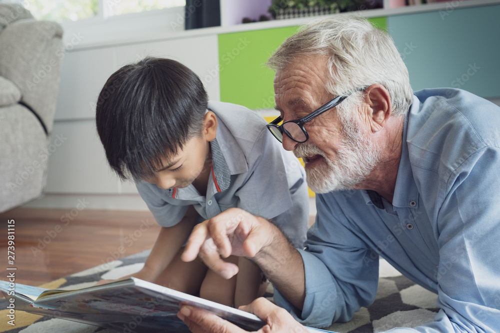 Obraz premium senior man happiness and grandson are sitting on the floor and playing games and reading book at living room together