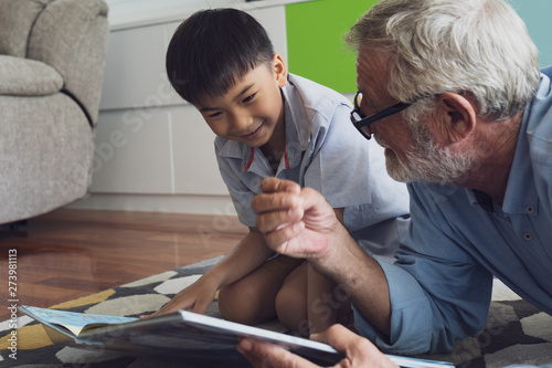 senior man happiness and grandson are sitting on the floor and playing games and reading book at living room together