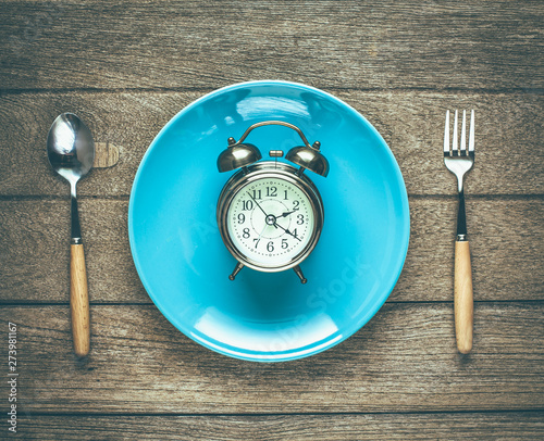 One vintage clock in blue ceramic dish with fork and spoon on wood table top view. photo