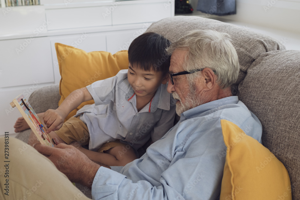 Obraz premium senior man happiness and grandson are sitting on the sofa and playing games and reading book at living room together