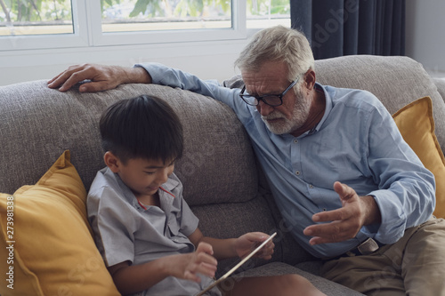 senior man happiness and grandson are sitting on the sofa and playing games and using tablet at living room together