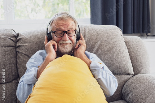 senior man happiness sitting on the sofa and listening music with headphone at living room for relaxing