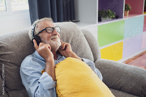 senior man happiness sitting on the sofa and listening music with headphone at living room for relaxing